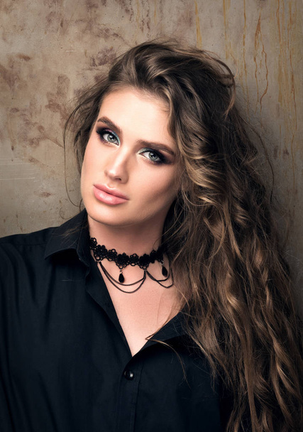 Vertical closeup portrait of young beautiful woman in black shirt posing in front of a metal wall - Foto, immagini