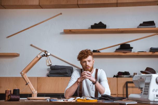 stijlvolle jonge mannelijke modeontwerper zittend aan tafel op werkplek - Foto, afbeelding