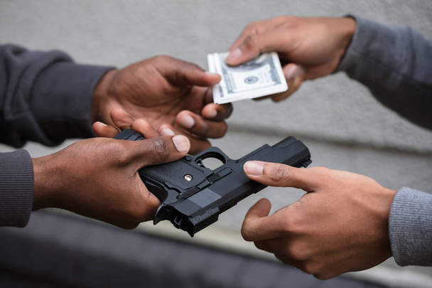 Close-up Of Two Hands Exchanging Black Handgun For Banknote - Photo, Image