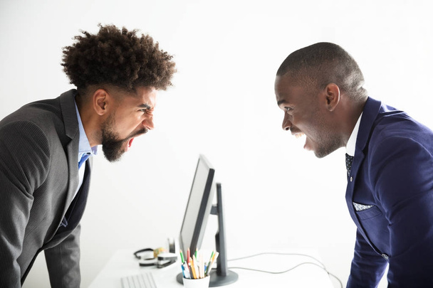Two Angry Young Businessmen Shouting At Each Other At Workplace - Фото, изображение