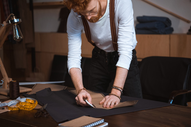 концентрированный молодой дизайнер мужской одежды в очках, работающий с узором шитья в мастерской
  - Фото, изображение
