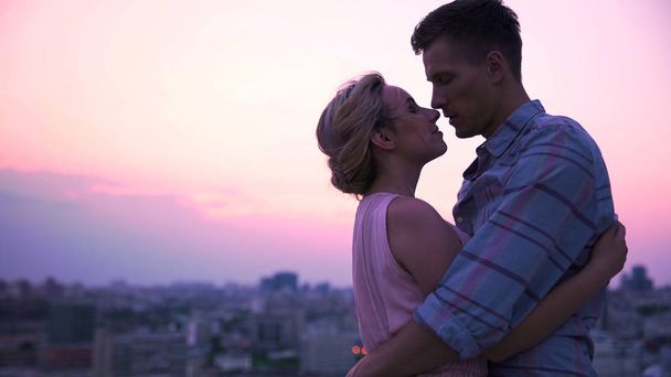 Handsome guy tenderly embracing his beautiful lady on open terrace, cityscape - Photo, image