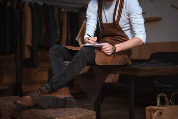 tiro recortado de designer de moda masculina em avental tomar notas no notebook
 - Foto, Imagem