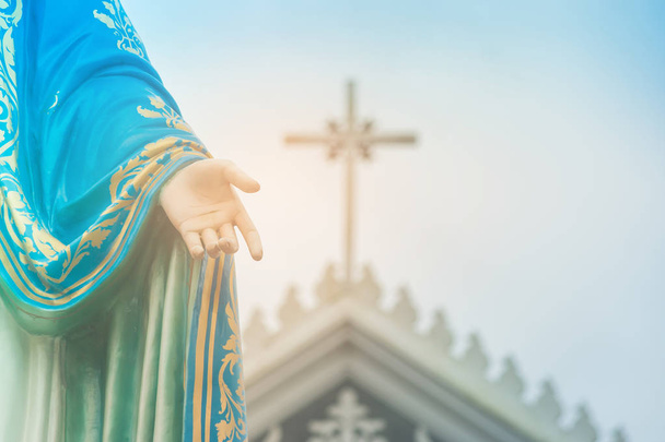 Рука статуи Пресвятой Девы Марии, стоящей перед Римско-католической епархией с распятием или крестом и голубым небом на заднем плане в провинции Чантхабури, Таиланд
. - Фото, изображение