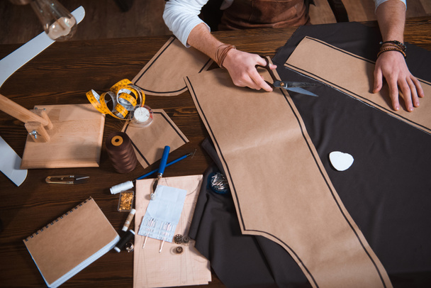 Schnappschuss eines männlichen Modedesigners, der am Arbeitsplatz mit Schnittmustern, Werkzeugen und Stoff arbeitet   - Foto, Bild