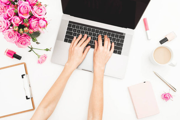 Meisje die op laptop werkt. Office werkruimte met vrouwelijke handen, laptop, roze rozen boeket, koffiemok, dagboek op witte tafel. Bovenaanzicht. Plat leggen. - Foto, afbeelding