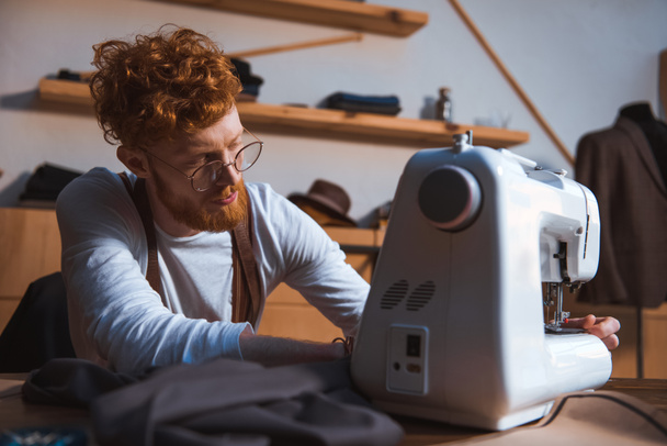 ориентированный молодой дизайнер в очках, работающий с швейной машинкой
 - Фото, изображение