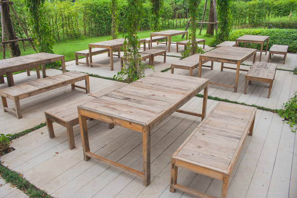 Muchas filas de sillas de madera y mesa en un hermoso jardín al aire libre rodeado de verde natural
. - Foto, Imagen