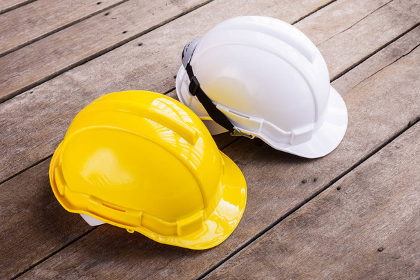 желтый, белый жесткий шлем безопасности строительная шляпа для проекта безопасности рабочего в качестве инженера или рабочего, инженерно-строительного оборудования, на деревянном полу
 - Фото, изображение