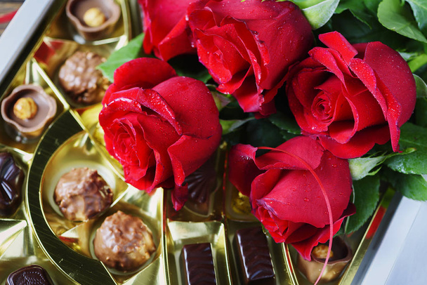 Composition with red roses and chocolate candies on wooden background - Fotó, kép