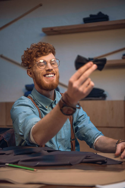 uśmiechnięty młody mężczyzna projektant mody w okularach gospodarstwa muszką - Zdjęcie, obraz