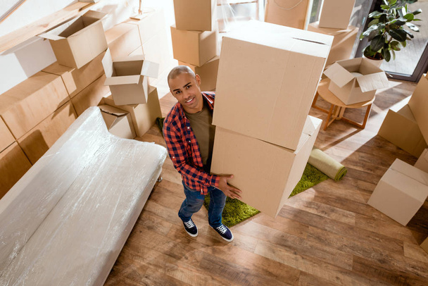 young african american man holding cardboard box and moving into new home - Foto, afbeelding