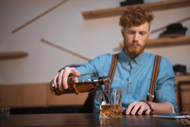 close-up view of young man pouring whisky from bottle in glass - Foto, imagen