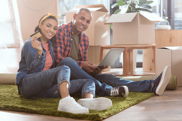 Afrikanisch-amerikanisches Paar kauft online mit Kreditkarte und Laptop in neuer Wohnung mit Kartons ein - Foto, Bild