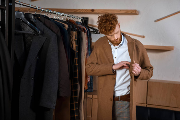 handsome young man wearing brown overcoat in boutique  - Φωτογραφία, εικόνα