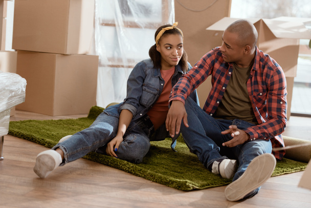 Африканская пара сидит на полу в новой квартире с картонными коробками
 - Фото, изображение