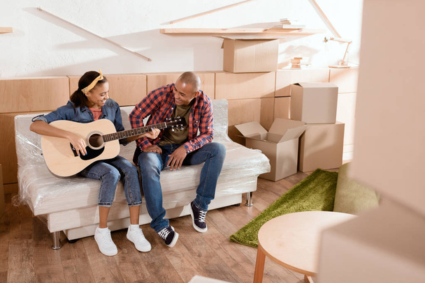 Afrikaanse Amerikaanse echtpaar spelen op akoestische gitaar in de nieuwe woning met kartonnen dozen - Foto, afbeelding