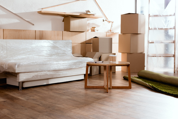 sofa, tafel, warmgewalste tapijt en kartonnen dozen in nieuw appartement - Foto, afbeelding