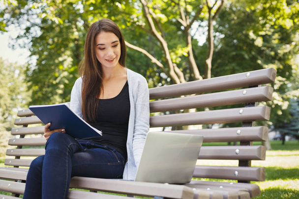 Smiling student girl sitting in park using laptop - Foto, Bild
