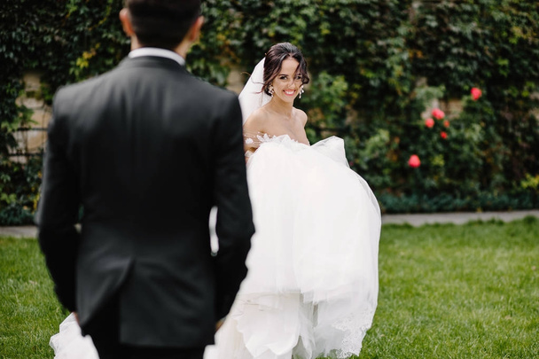 Happy smiling stylish bride and groom walking in the summer green park with bouquet of flowers, dancing and having fun on the their wedding day - Foto, imagen