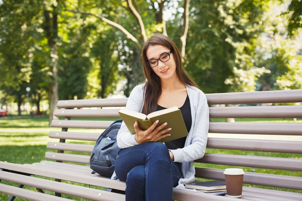 Young woman reading book in park copy space - Fotó, kép