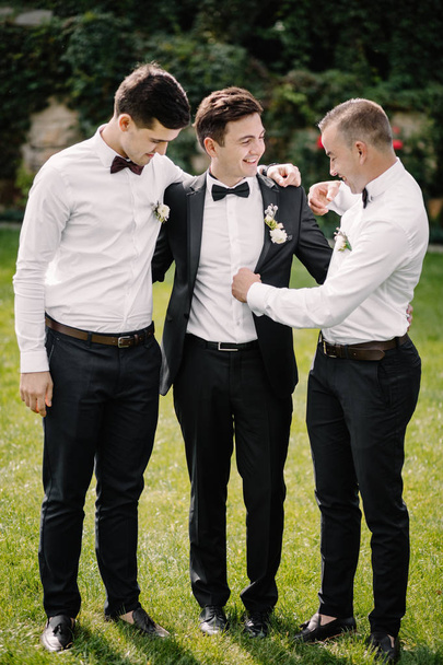 Laughing groomsmen in suits holding smiling groom under his arms - Fotó, kép