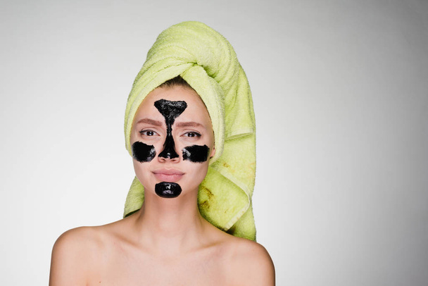 a cute young girl with a green towel on her head applied a black mask to the problem zones on her face - Valokuva, kuva