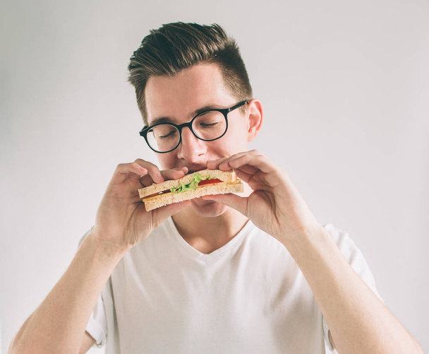 man holding a piece of hamburger. student eats fast food. not helpful food. very hungry man. Nerd is wearing glasses. - Fotó, kép