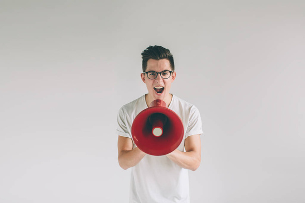 portrait of young man shouting using megaphone over background Nerd is wearing glasses. - Photo, Image
