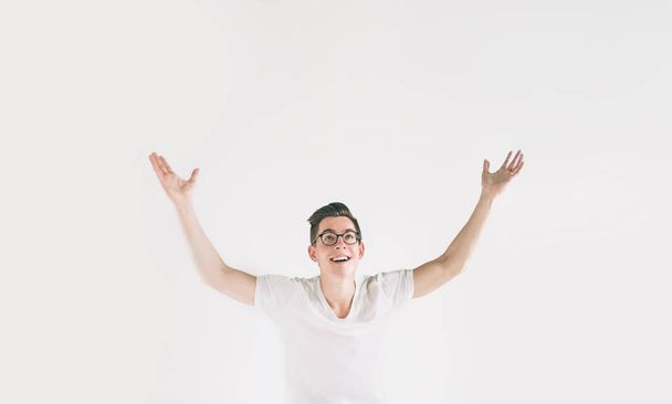 Young happy man with in casuals with raised hands up isolated on white background. Nerd is wearing glasses. - Foto, afbeelding
