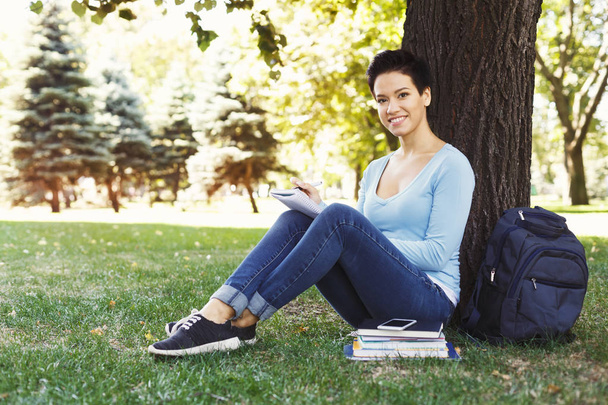 Jeune femme assise avec un cahier sur l'herbe
 - Photo, image
