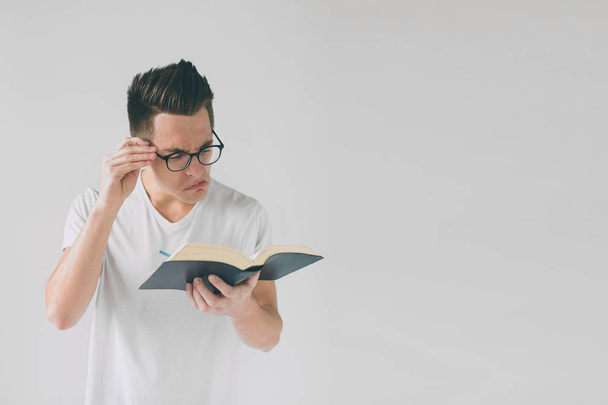 nerd with glasses and a white t-shirt is reading a book on a white background - Photo, image