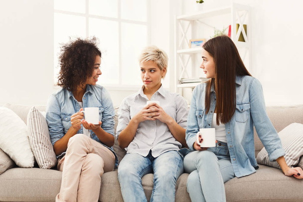 Three young female friends with coffee chatting at home - Фото, зображення
