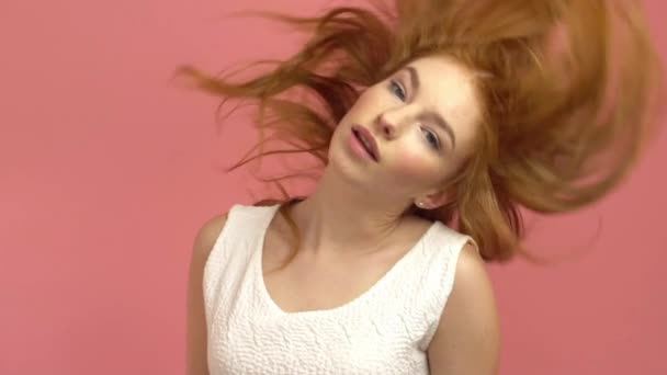 Beautiful teenage girl with red blowing hair and blue eyes on pink background - 映像、動画