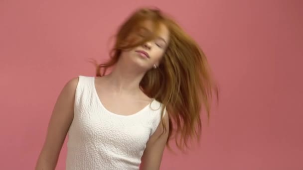 Beautiful teenage girl with red blowing hair and blue eyes on pink background - Filmati, video