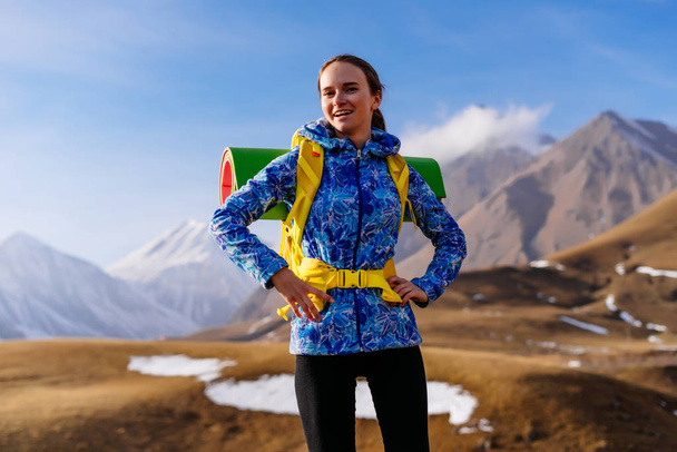 young happy girl in a blue jacket travels along the Caucasian ridge with a backpack and tent - Foto, Imagem