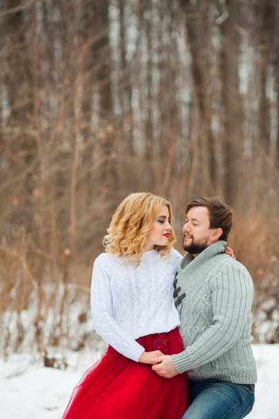 beautiful young couple in love in sweaters walking on snowy forest park - Фото, изображение