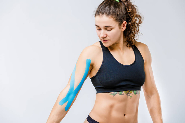 Concept of sports medicine and health. beautiful girl with good figure posing on gray background with kinesiology tape,a sticky blue ribbon on her arm.Alternative medicine for stretching and pain - Foto, afbeelding
