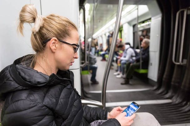Νεαρό κορίτσι ανάγνωση από την οθόνη του κινητού τηλεφώνου στο μετρό. - Φωτογραφία, εικόνα