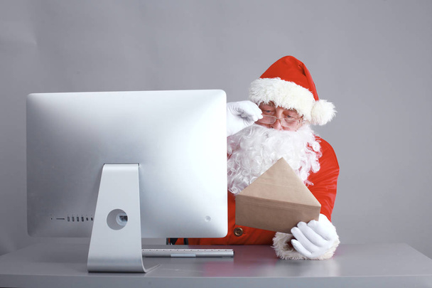 Santa Claus reading children letters and writing responses to them using laptop . - Fotografie, Obrázek