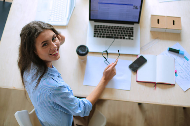Nuori nainen istuu toimistopöydässä ja katselee kannettavan tietokoneen näyttöä. Nuori nainen - Valokuva, kuva