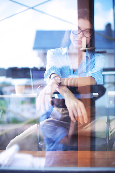 Young woman sitting at office table with laptop,view through window. Young woman - 写真・画像