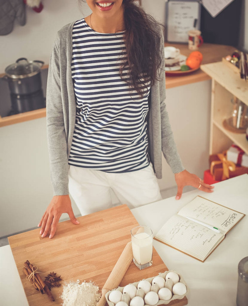 Smiling young woman in the kitchen, isolated on christmas background - Foto, afbeelding