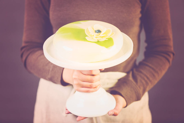 Pastre chef tenant gâteau de mousse gastronomique sur un stand de gâteau blanc
. - Photo, image