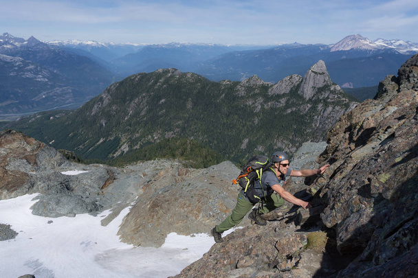 A Fit Young Caucasian Adventurous Man is climbing a steep rock slab during a beautiful summer day. Picture taken on the ascent to Skypilot Mountain near Squamish, North of Vancouver, BC, Canada. - Фото, зображення