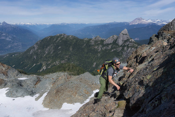 A Fit Young Caucasian Adventurous Man is climbing a steep rock slab during a beautiful summer day. Picture taken on the ascent to Skypilot Mountain near Squamish, North of Vancouver, BC, Canada. - Foto, Imagem