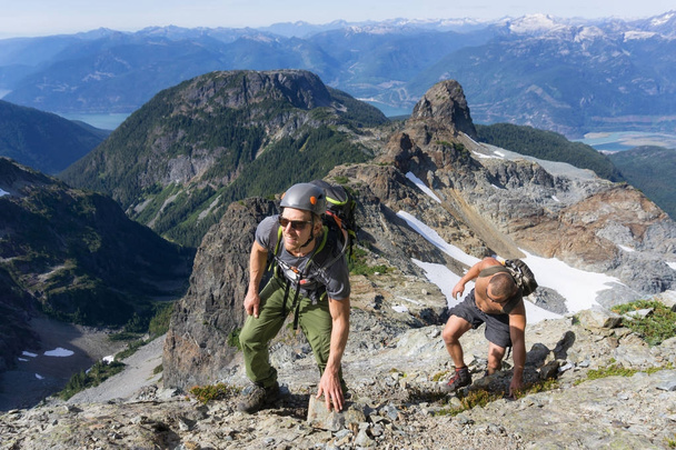 A couple of adventurous friends are hiking up a steep rock slab during a sunny summer day. Picture taken on the ascent to Skypilot Mountain near Squamish, North of Vancouver, BC, Canada. - 写真・画像