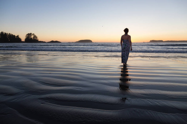 Rear view of the woman walking in the water of the ocean at sunset time  - Photo, image