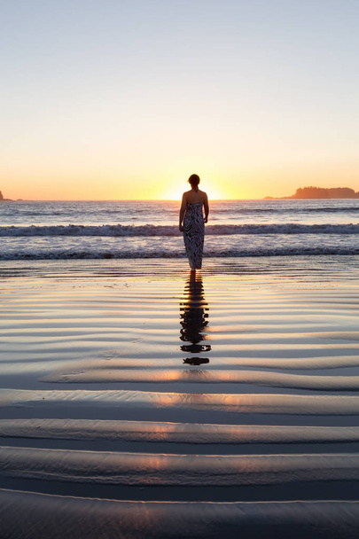 Rear view of the woman walking in the water of the ocean at sunset time  - Foto, afbeelding