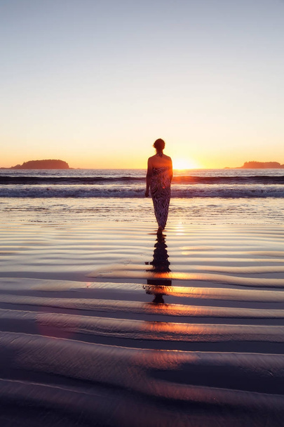 Вид ззаду жінки, що ходить у воді океану під час заходу сонця
  - Фото, зображення